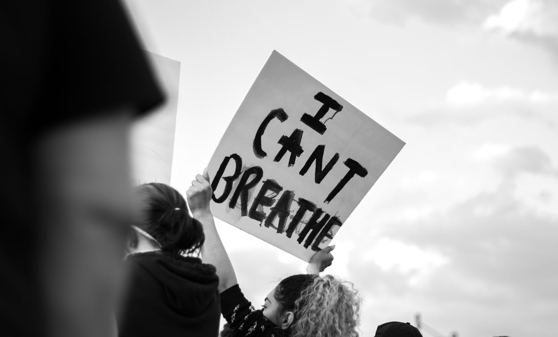 Woman holding a
                      sign with 'I can't Breathe' written on it